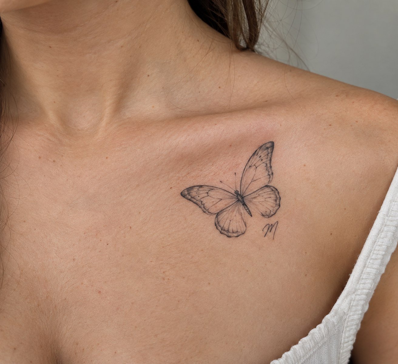 Fine-line memorial butterfly tattoo with a small initial.