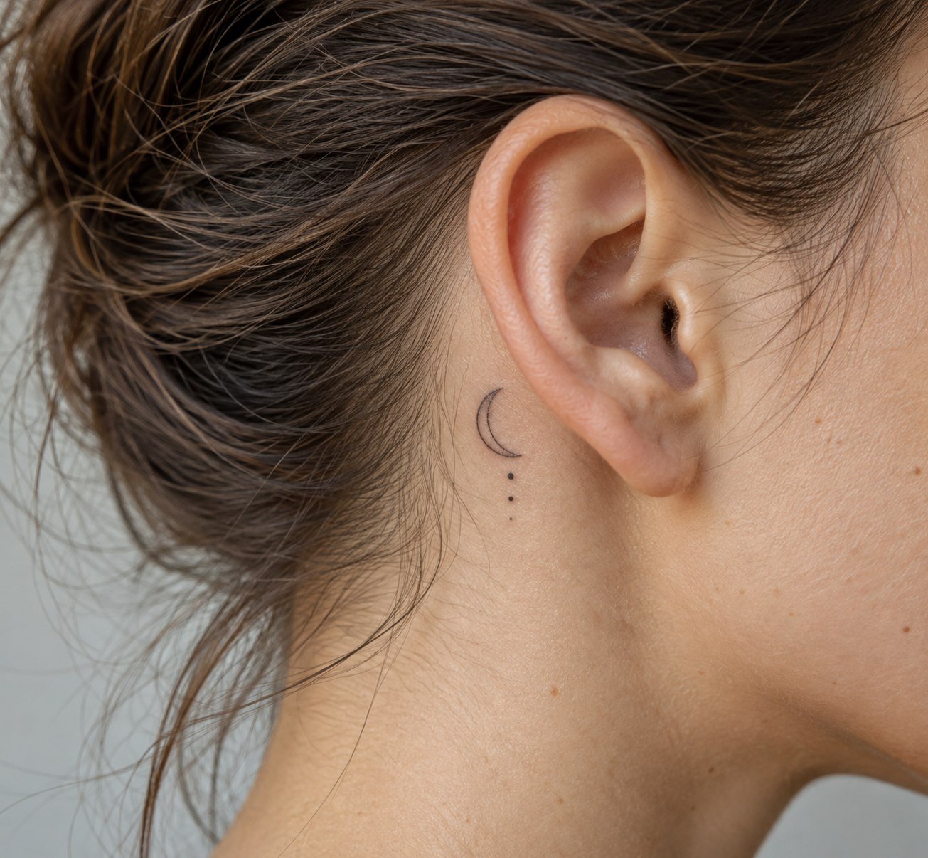 Tiny crescent moon tattoo with dot accents behind the ear.