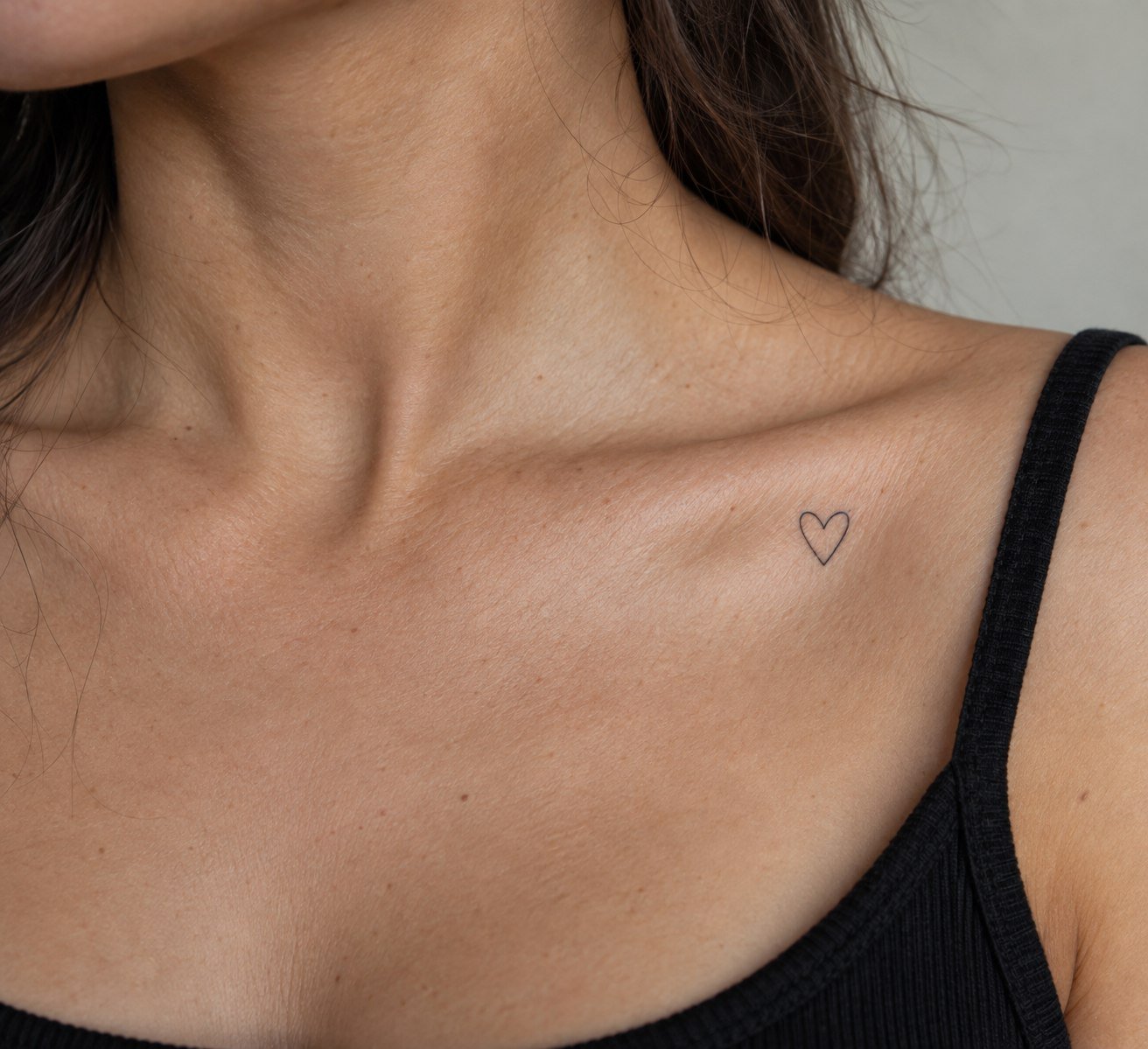 Delicate open-outline heart tattoo on the collarbone.