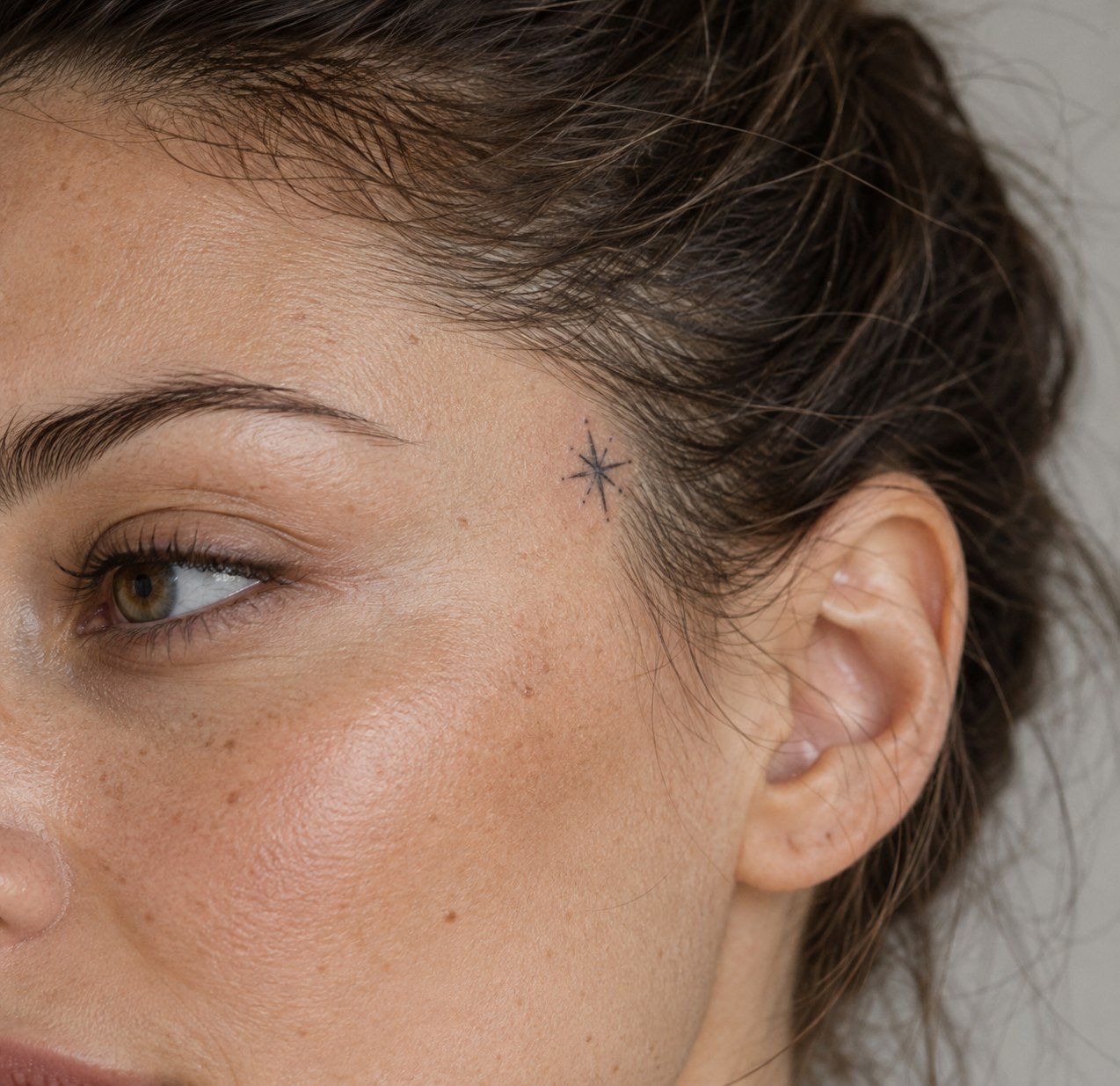 Small star tattoo near the temple hairline.