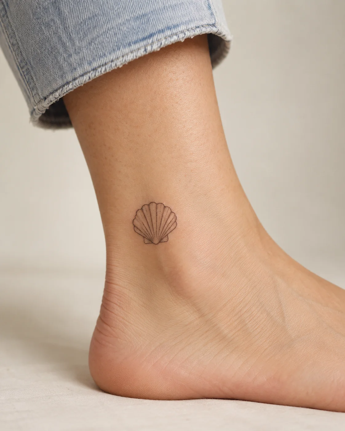 Small Seashell fine line tattoo concept on the outer ankle