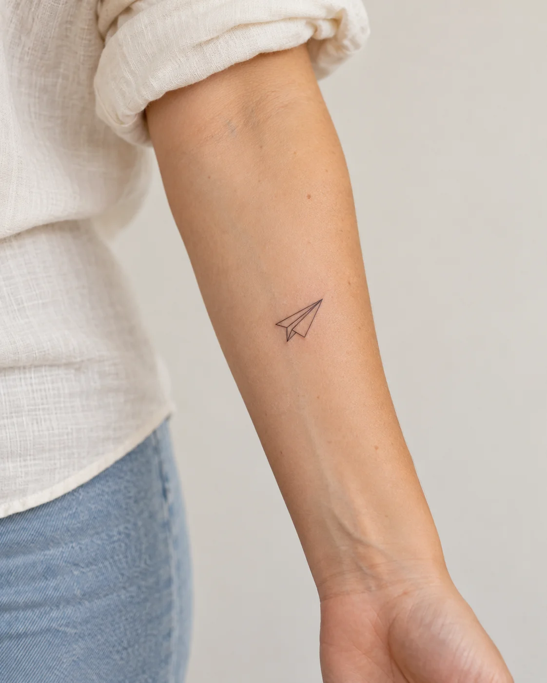 Tiny Paper Airplane fine line tattoo concept on the inner forearm